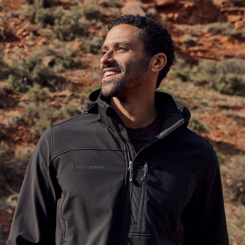 Man wearing a black hooded softshell jacket standing in a desert landscape